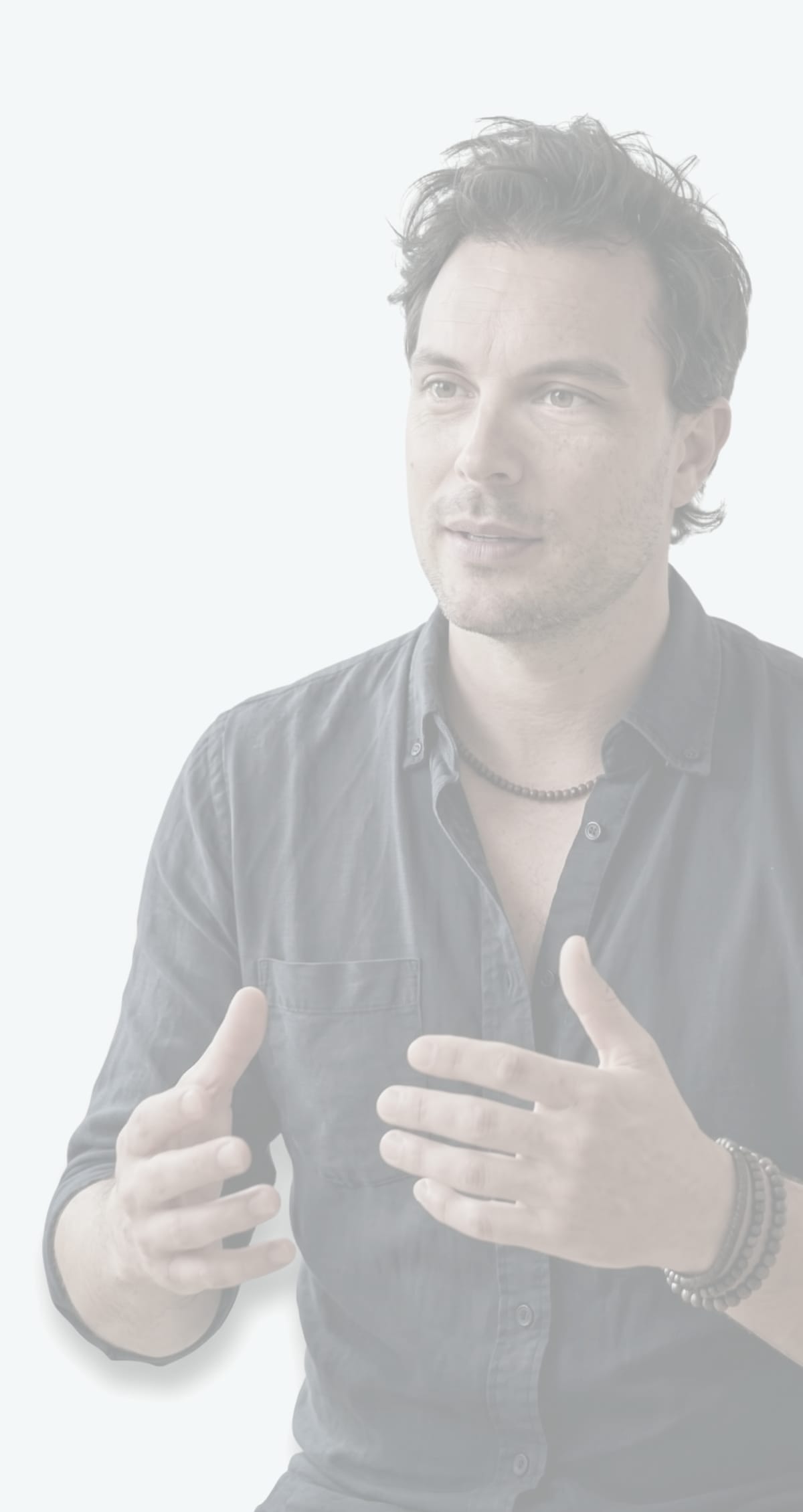 Man in a dark linen shirt gesturing with both hands as he speaks, cut out from his background